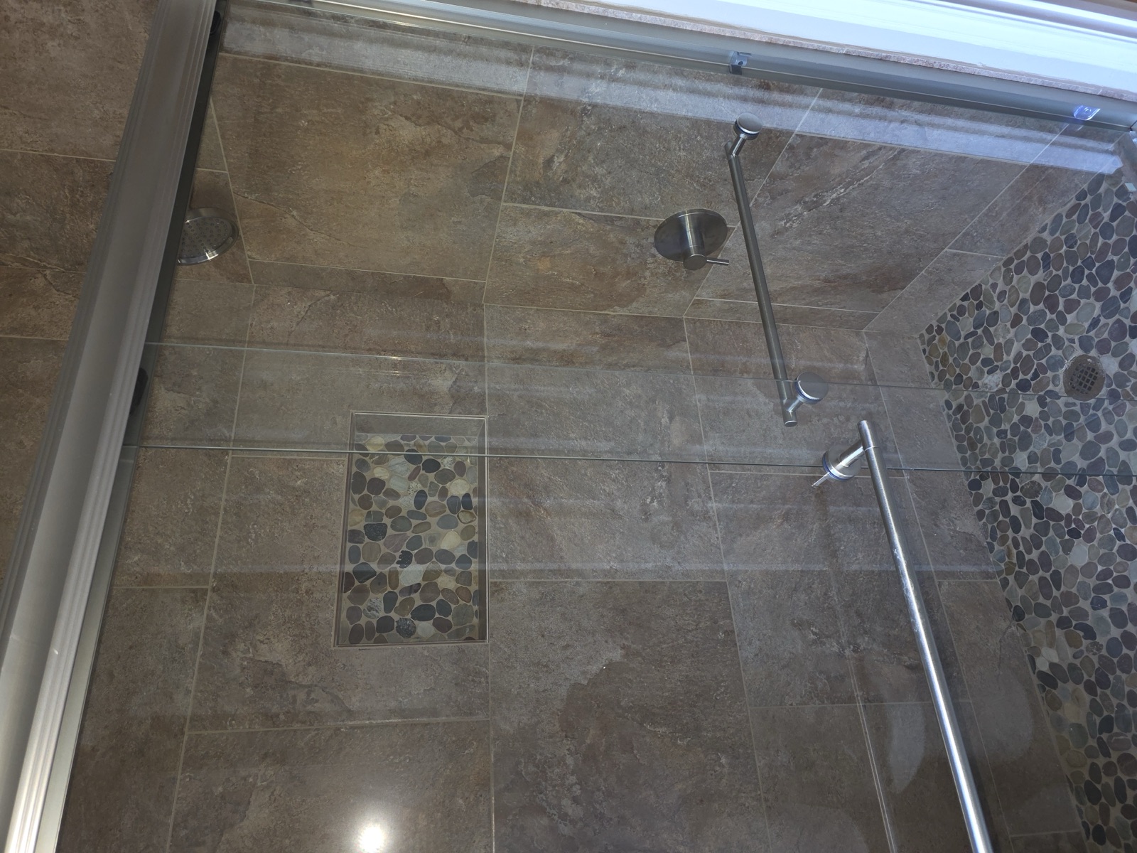Custom slate tile walk-in shower with glass doors and pebble mosaic niche